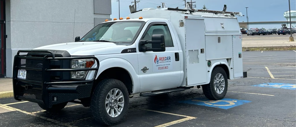 A white work truck with "Reeder" logo parked in a parking lot outside a building with a green awning.